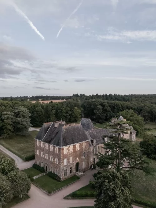 Aerial view of Château de Pordor surrounded by green countryside under a pale evening sky.