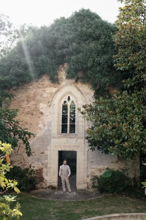 Groom standing beneath an ivy-covered archway of Château de Pordor’s historic chapel ruin.