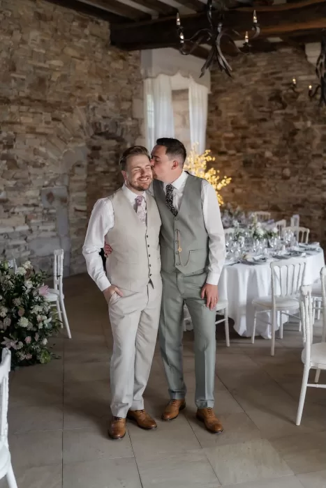 Grooms sharing a quiet moment in the softly lit reception room of Château de Pordor, surrounded by elegant table settings.