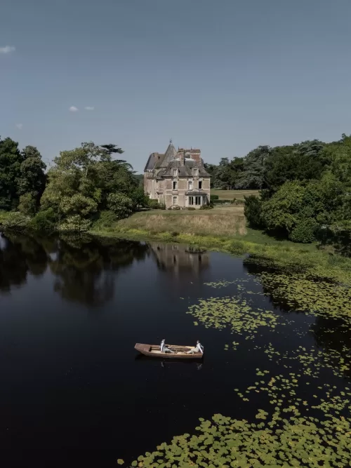 The grooms in a wooden rowboat on the tranquil lake beside Château de Pordor surrounded by lily pads.