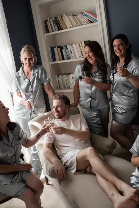 Groom relaxing with friends in matching silk pajamas while sharing champagne in a cozy room at Château de Pordor.