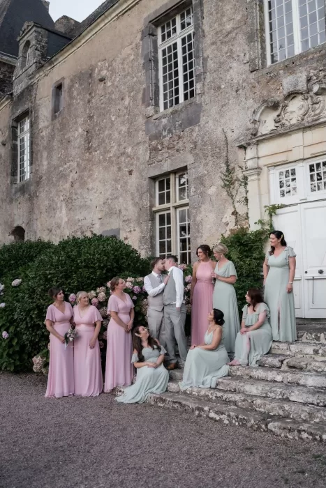 The newlyweds with their wedding party in pastel dresses gathered on the stone steps of Château de Pordor.