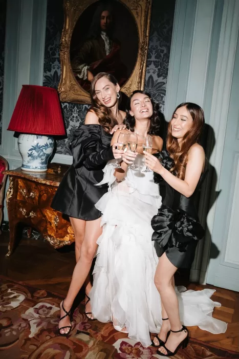 Bride laughing with bridesmaids in black dresses while toasting champagne inside Château de Villette.