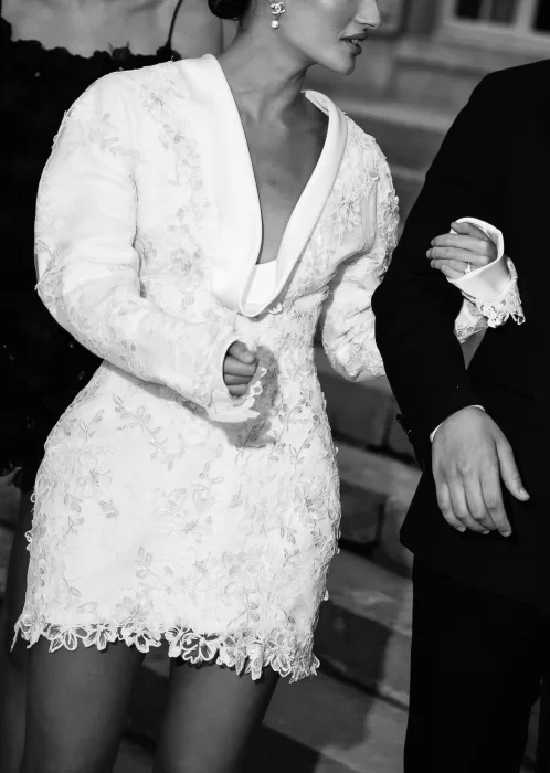 Bride in an embroidered mini dress with long sleeves walking arm in arm with the groom at Château de Villette.