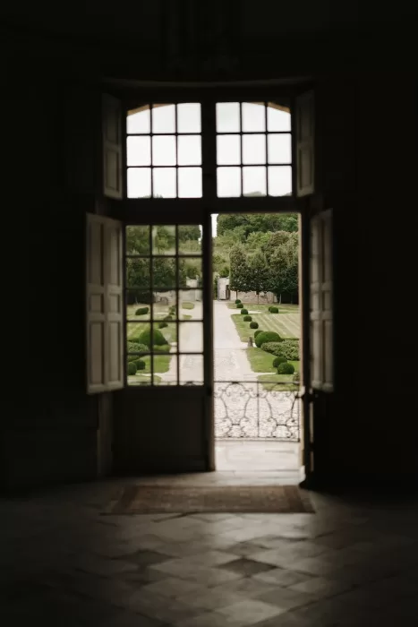 View through open French doors at Château de Villette, revealing the cobbled path and formal gardens beyond.