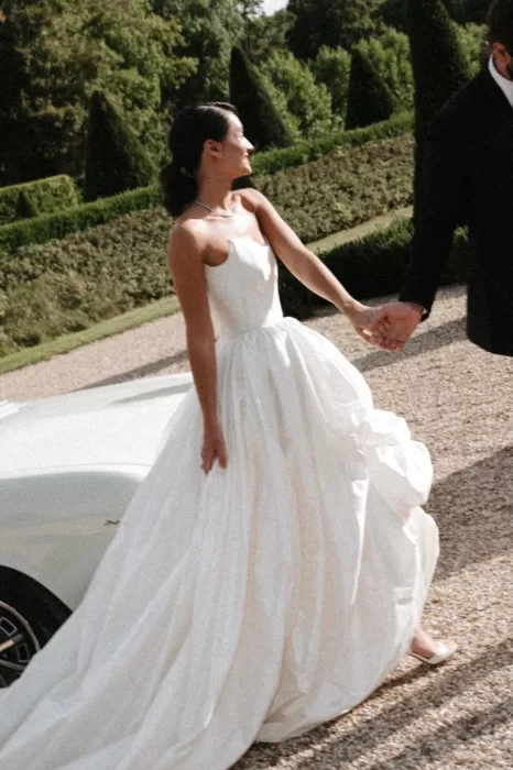 Bride smiling in the gardens of Château de Villette, holding her groom’s hand while her silk gown catches the sunlight.