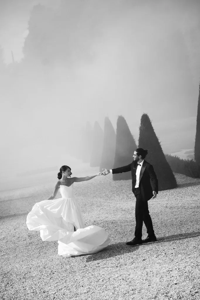 Bride and groom dancing amid ethereal smoke in the formal gardens of Château de Villette, captured in black and white.