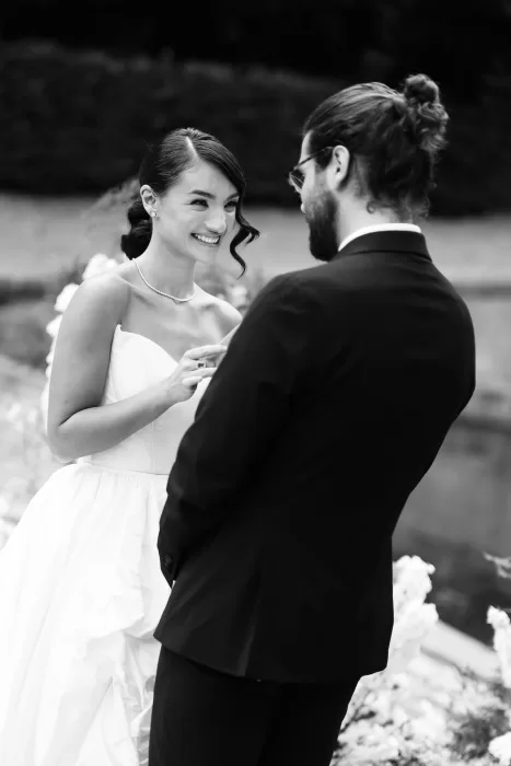 Bride smiling joyfully while exchanging rings with the groom during their outdoor ceremony at Château de Villette.