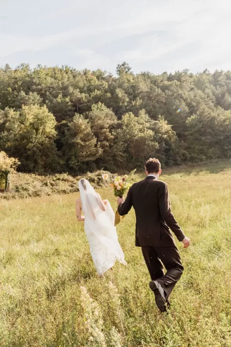 The bride and groom walking hand in hand through a sunlit meadow at This Must Be The Place.