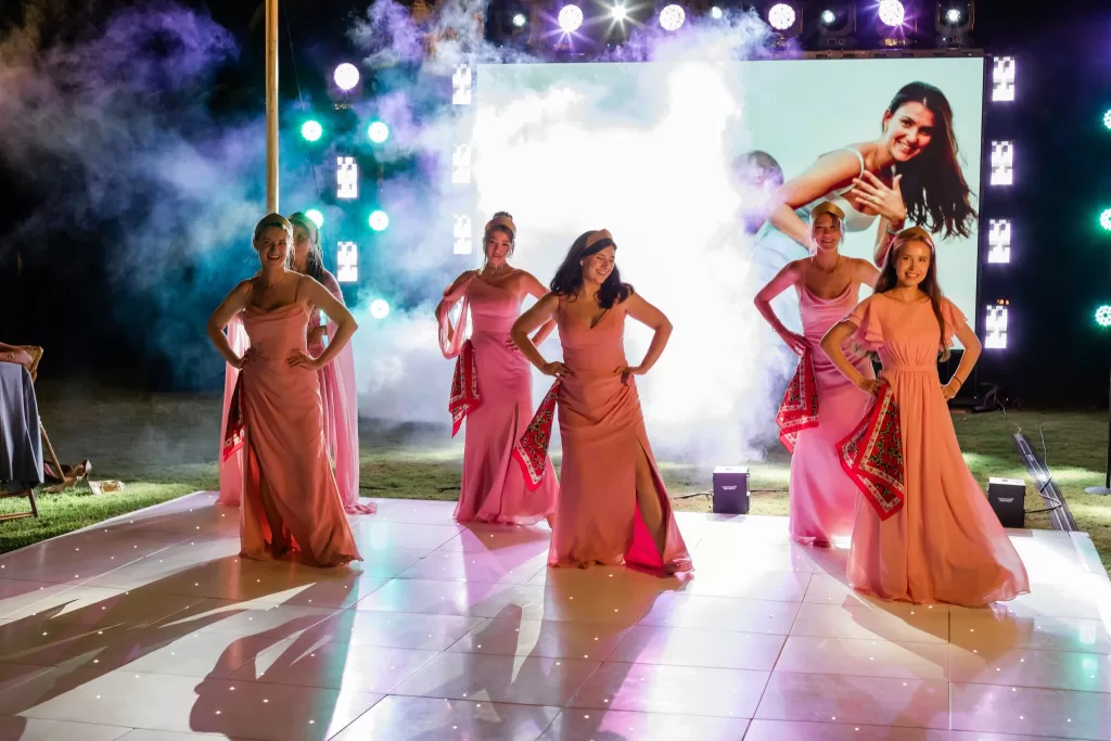 Bridesmaids in pink dresses perform a joyful dance under colorful stage lights during the evening reception at Finca la Concepción.