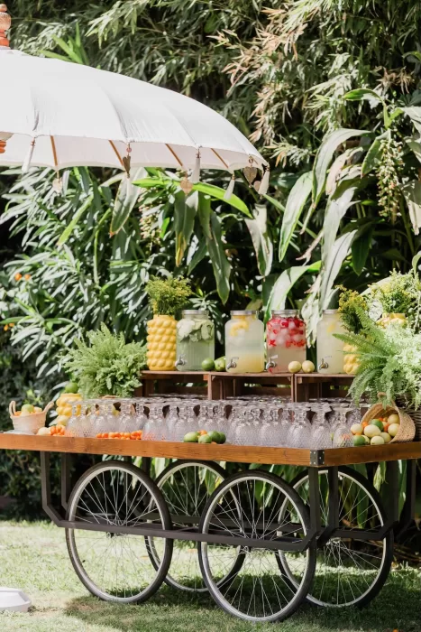 Refreshing citrus drink station at Finca la Concepción featuring glass dispensers, greenery, and a white parasol.