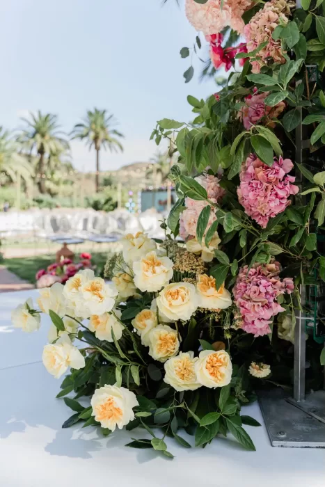 Close-up of peach and yellow blooms decorating the wedding arch at Finca la Concepción with palm trees in the background.