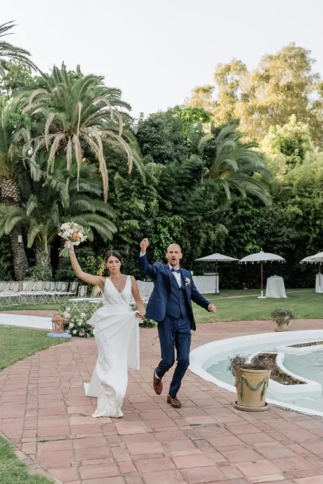 Bride and groom celebrating joyfully as they walk past the fountain at Finca la Concepción after their ceremony.