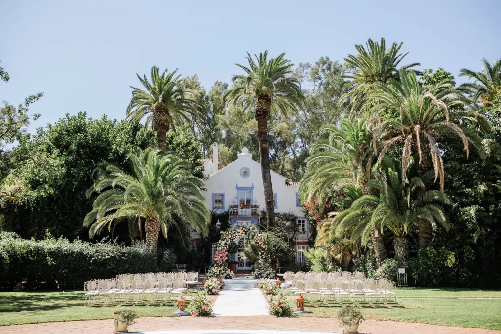 Grand view of Finca la Concepción’s white villa framed by tall palm trees and floral ceremony setup.