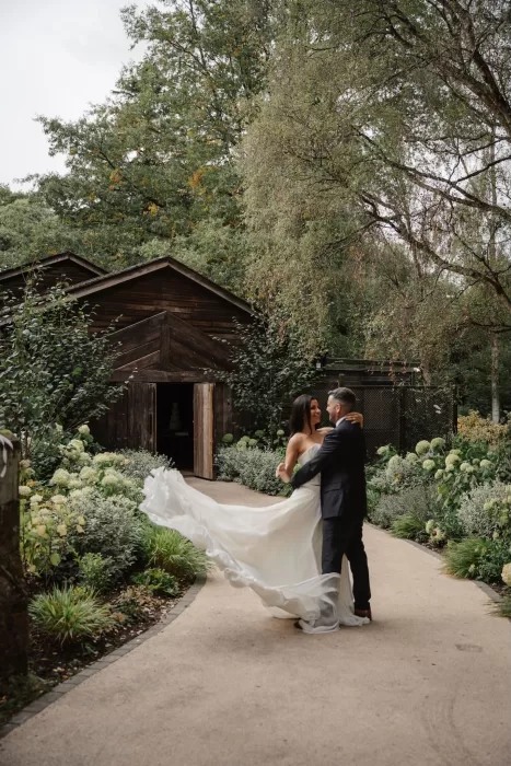 Bride and groom dancing outside the wooden barn at Hampton Manor surrounded by green gardens.