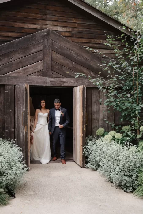 Couple exiting the rustic wooden barn surrounded by greenery at Hampton Manor.