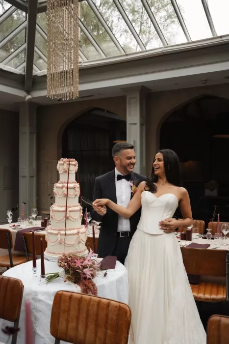 Newlyweds cutting a tall tiered cake together in the light-filled conservatory at Hampton Manor.