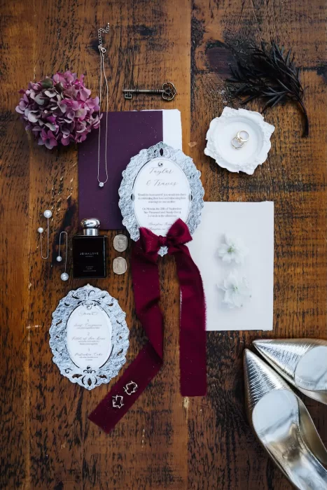 Elegant wedding flat lay at Hampton Manor featuring invitations, jewellery, perfume, and floral accents.