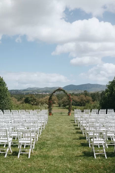 Outdoor ceremony arch framed by mountain views at Herdade do Peru, surrounded by rows of white chairs.