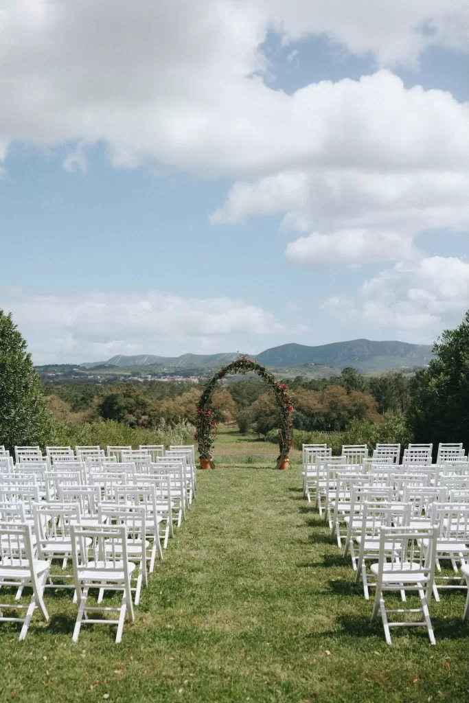 Outdoor ceremony arch framed by mountain views at Herdade do Peru, surrounded by rows of white chairs.