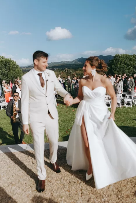 Bride and groom holding hands joyfully after their ceremony under blue skies at Herdade do Peru.