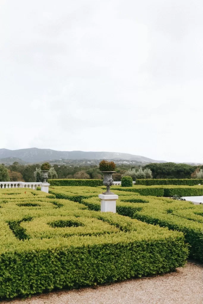 Manicured geometric hedges with stone urns and distant mountain views at Herdade do Peru gardens.