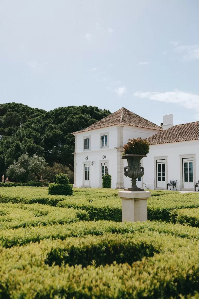 Elegant white manor overlooking manicured green hedges and scenic countryside at Herdade do Peru.