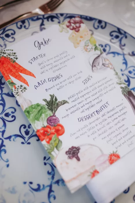 Hand-painted wedding menu with colorful fruit and vegetable illustrations on patterned blue china at Herdade do Peru.