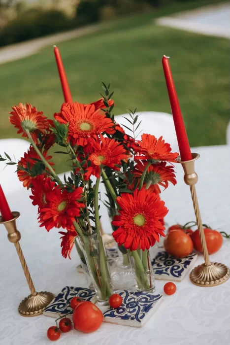 Vibrant red floral table decor with candles and tomatoes at Herdade do Peru, inspired by Mediterranean summer colors.