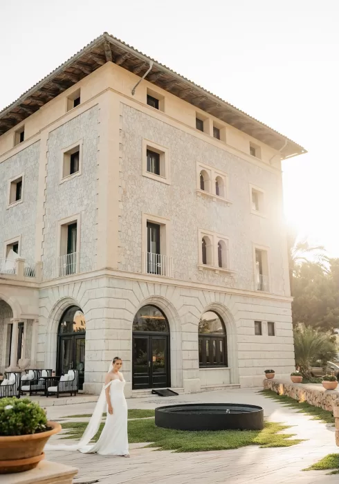 Bride standing gracefully in front of Hospes Maricel & Spa, bathed in golden hour sunlight.