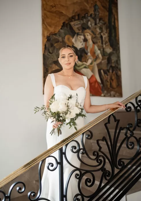 Bride holding a white bouquet descending the ornate staircase inside Hospes Maricel & Spa.