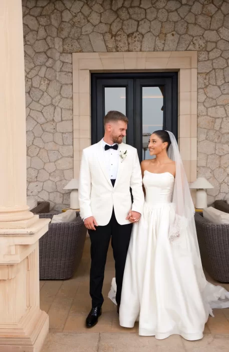 Newlyweds stand smiling in the stone courtyard of Hospes Maricel & Spa.