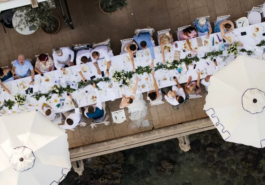 Overhead view of a long wedding dinner table at Hospes Maricel & Spa, with guests toasting under white umbrellas.