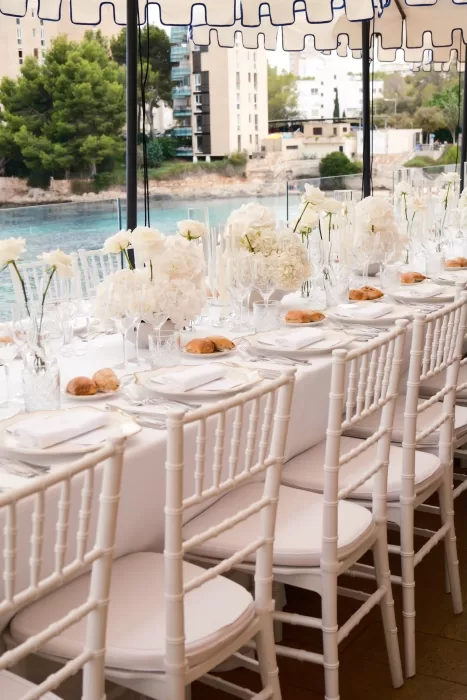 Elegant dinner setup with white chairs and floral centerpieces beside the water at Hospes Maricel & Spa.