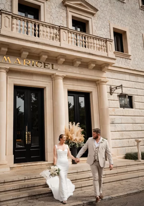 Newlyweds holding hands on the grand front steps of Hospes Maricel & Spa beneath its iconic stone entrance.