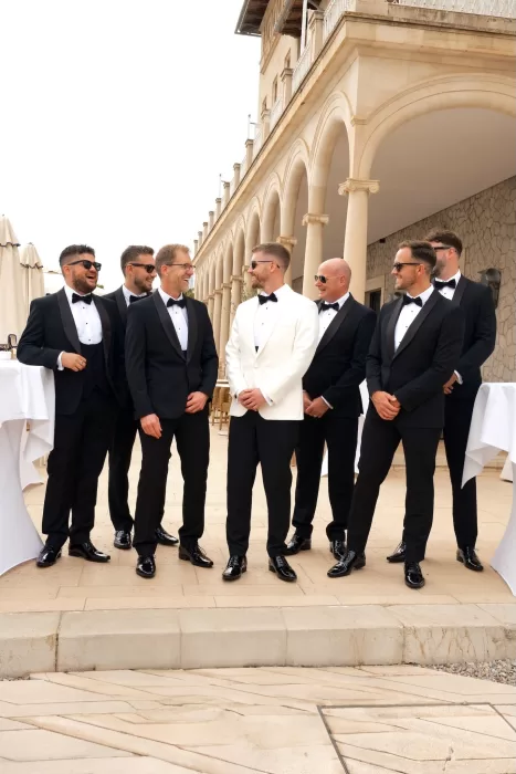 Groom and groomsmen in tuxedos share a laugh on the elegant terrace of Hospes Maricel & Spa.