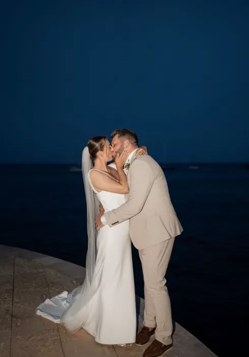Bride and groom share a romantic kiss by the water at dusk outside Hospes Maricel & Spa.