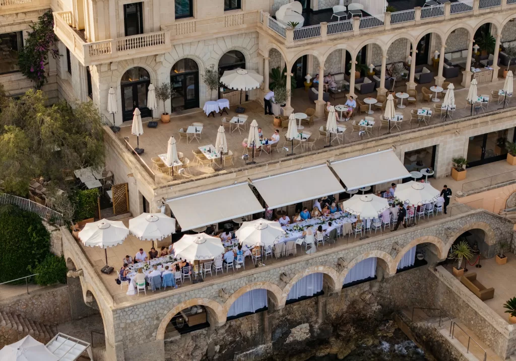 Aerial view of a wedding reception on the lower terrace of Hospes Maricel & Spa with guests dining by the sea.