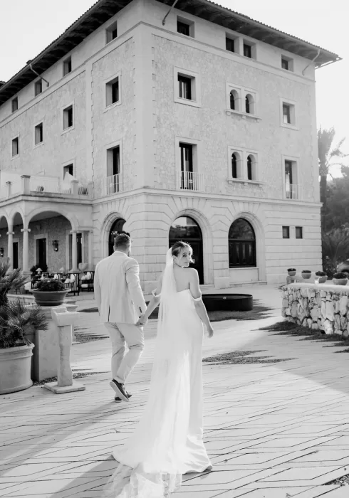 Bride and groom walking hand in hand outside Hospes Maricel & Spa, captured in elegant black and white.