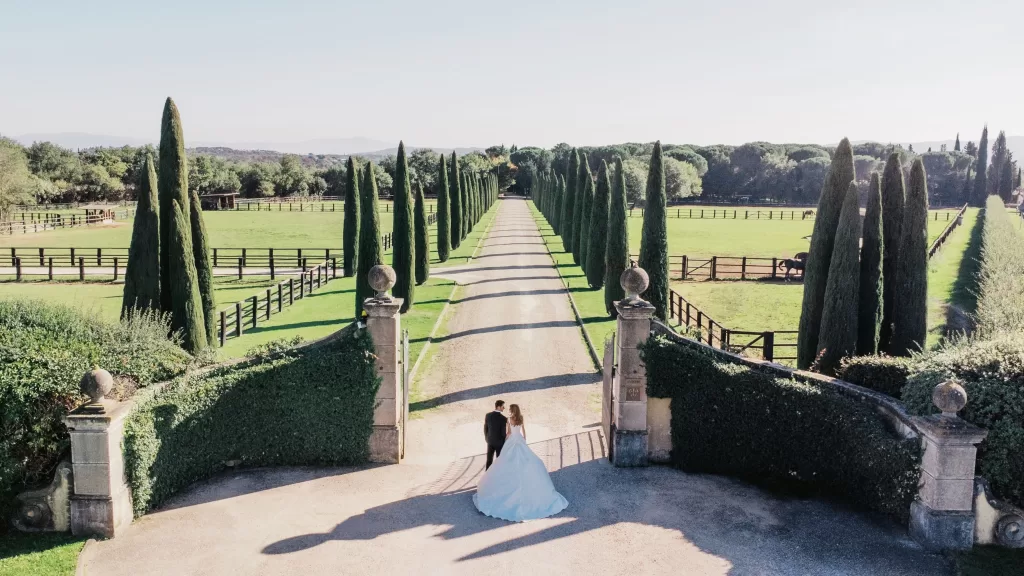 Aerial view of Il Borro’s sweeping cypress-lined driveway with newlyweds at the gate, surrounded by Tuscan fields.