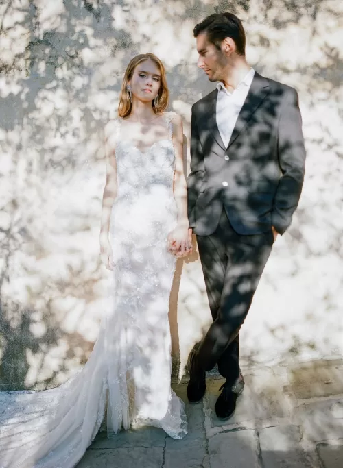 Bride and groom standing close in dappled sunlight against a stone wall at Il Borro, softly romantic atmosphere.