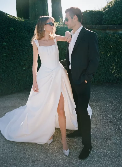 Stylish bride and groom in modern black-tie attire share a relaxed moment in Il Borro’s sunlit gardens.