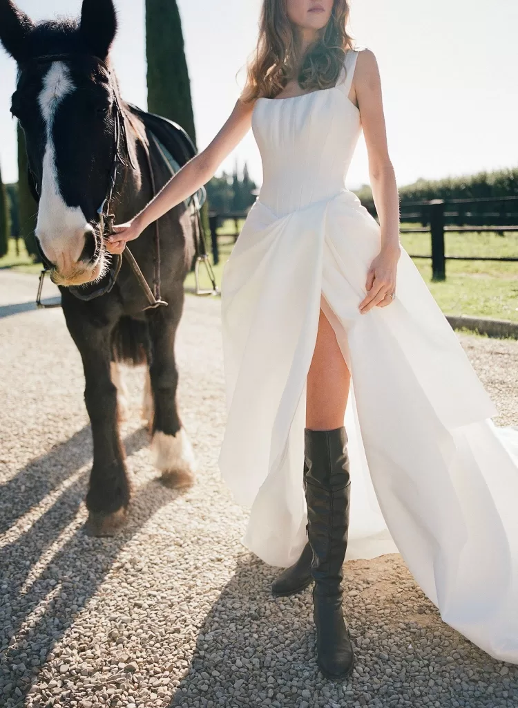 Bride in a modern white gown holding her horse’s reins at Il Borro, blending equestrian elegance with romance.