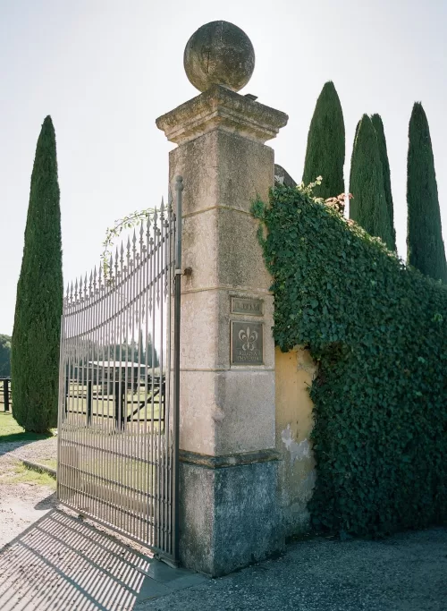 The grand wrought-iron gate at Il Borro framed by tall cypress trees and ivy-covered stone pillars in Tuscany.
