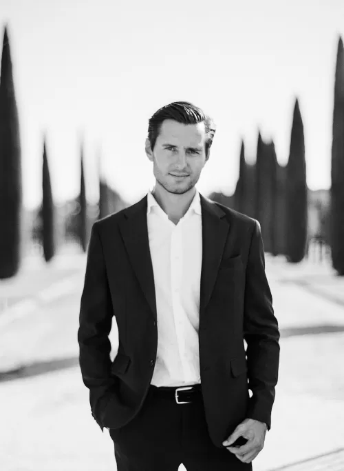 Groom in classic suit standing along Il Borro’s cypress-lined avenue, captured in timeless black and white.