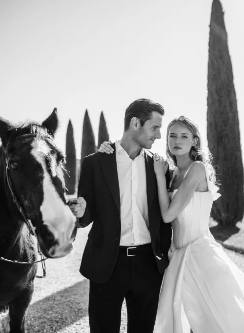 Black and white portrait of couple with their horse along Il Borro’s tree-lined path, full of timeless elegance.