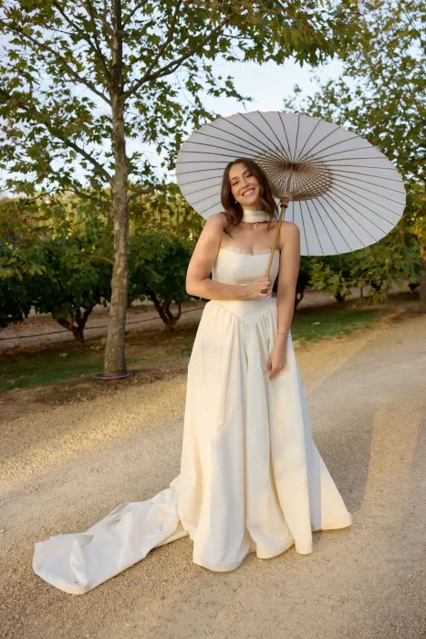 Bride in flowing gown holding a white parasol on the tree-lined path at Le Mas Barossa.