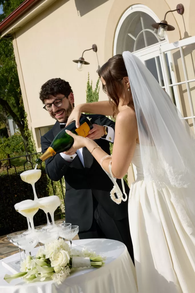 Newlyweds pouring champagne into coupe tower outside Le Mas Barossa villa.