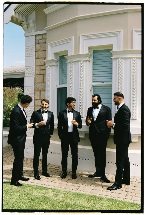 Groomsmen in tuxedos sharing a laugh outside the historic villa at Le Mas Barossa.