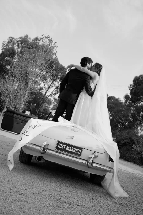 Newlyweds kissing on vintage car with “Just Married” sign at Le Mas Barossa.